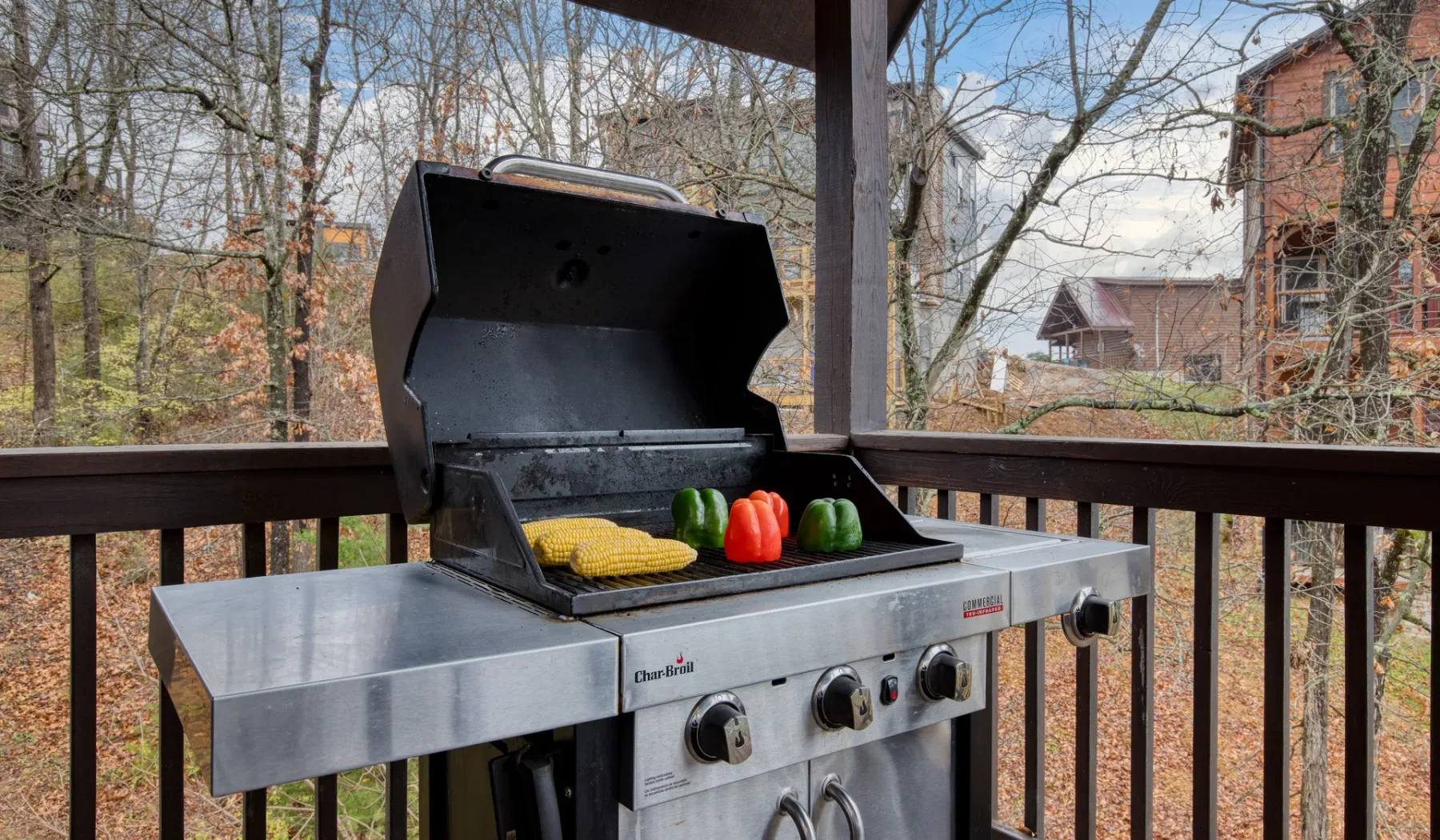 Una parrilla de gas con maíz y verduras está en una terraza cubierta.