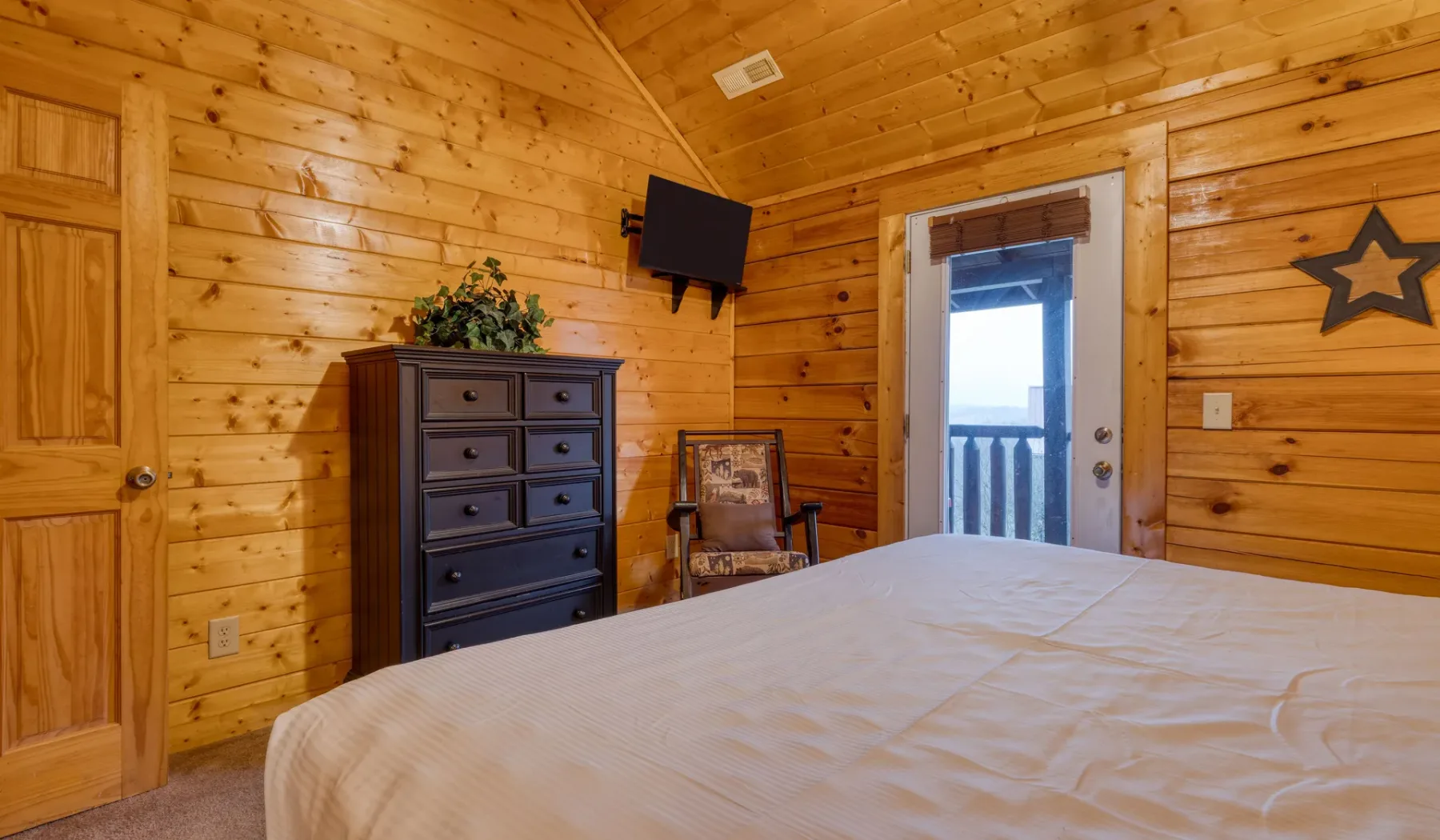 Dormitorio con paredes de madera, cama, cómoda y una puerta que da a un balcón.