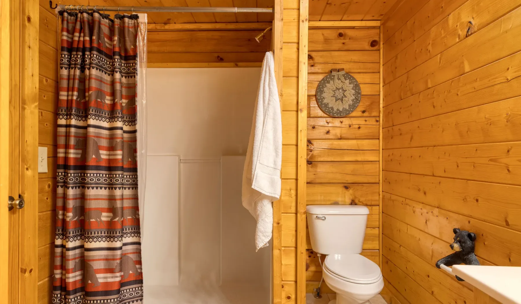Un baño revestido de madera con ducha, inodoro y lavabo.