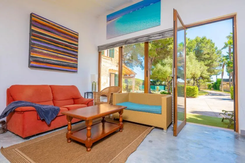 A bright living room has orange seating beside an open glass door to a garden.