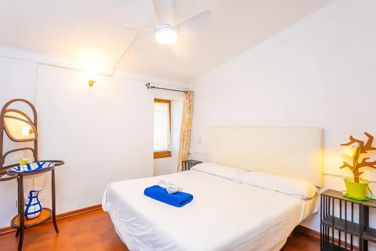 A bright bedroom with a bed, a small window, and bedside lighting.