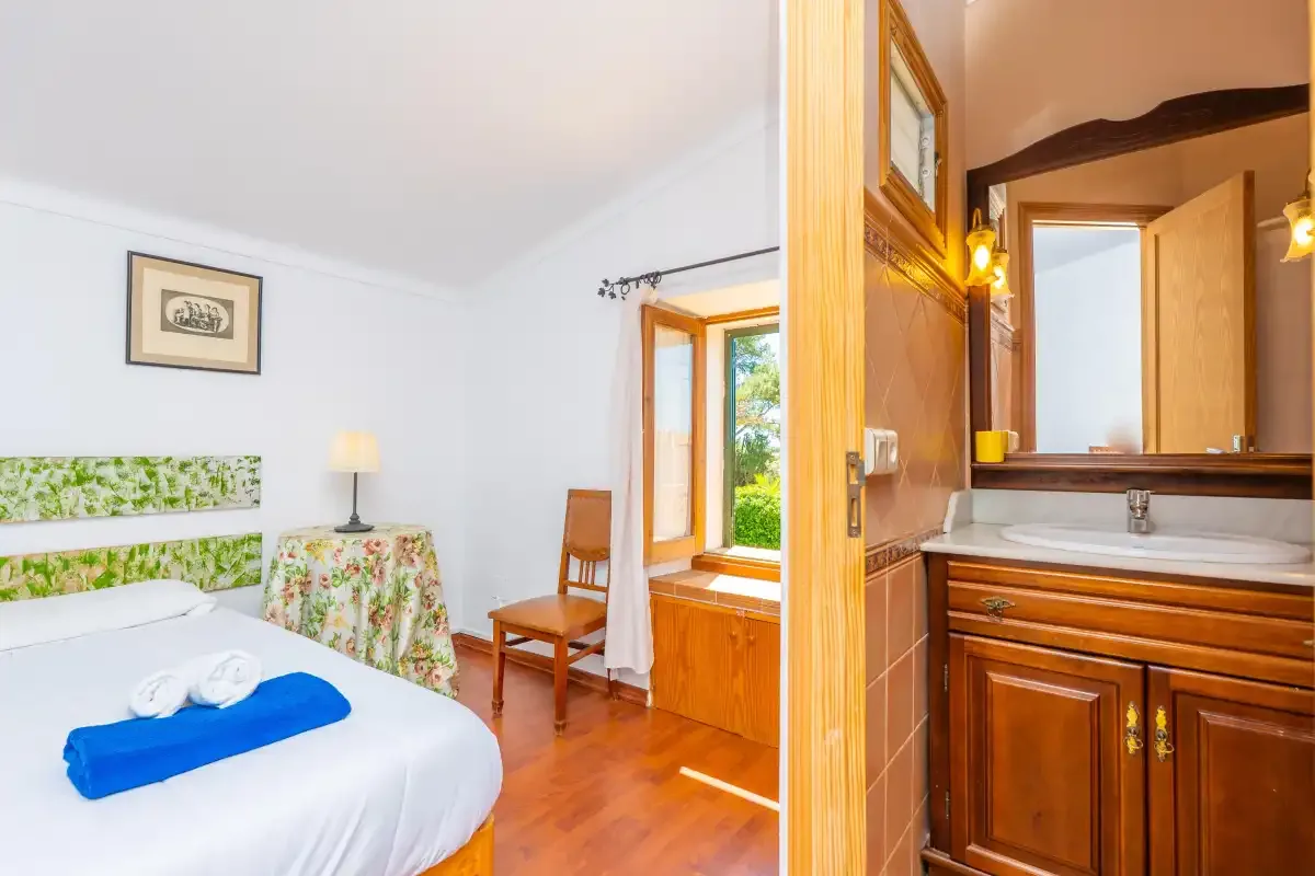 A bedroom with a bed beside an open window and a wooden vanity.