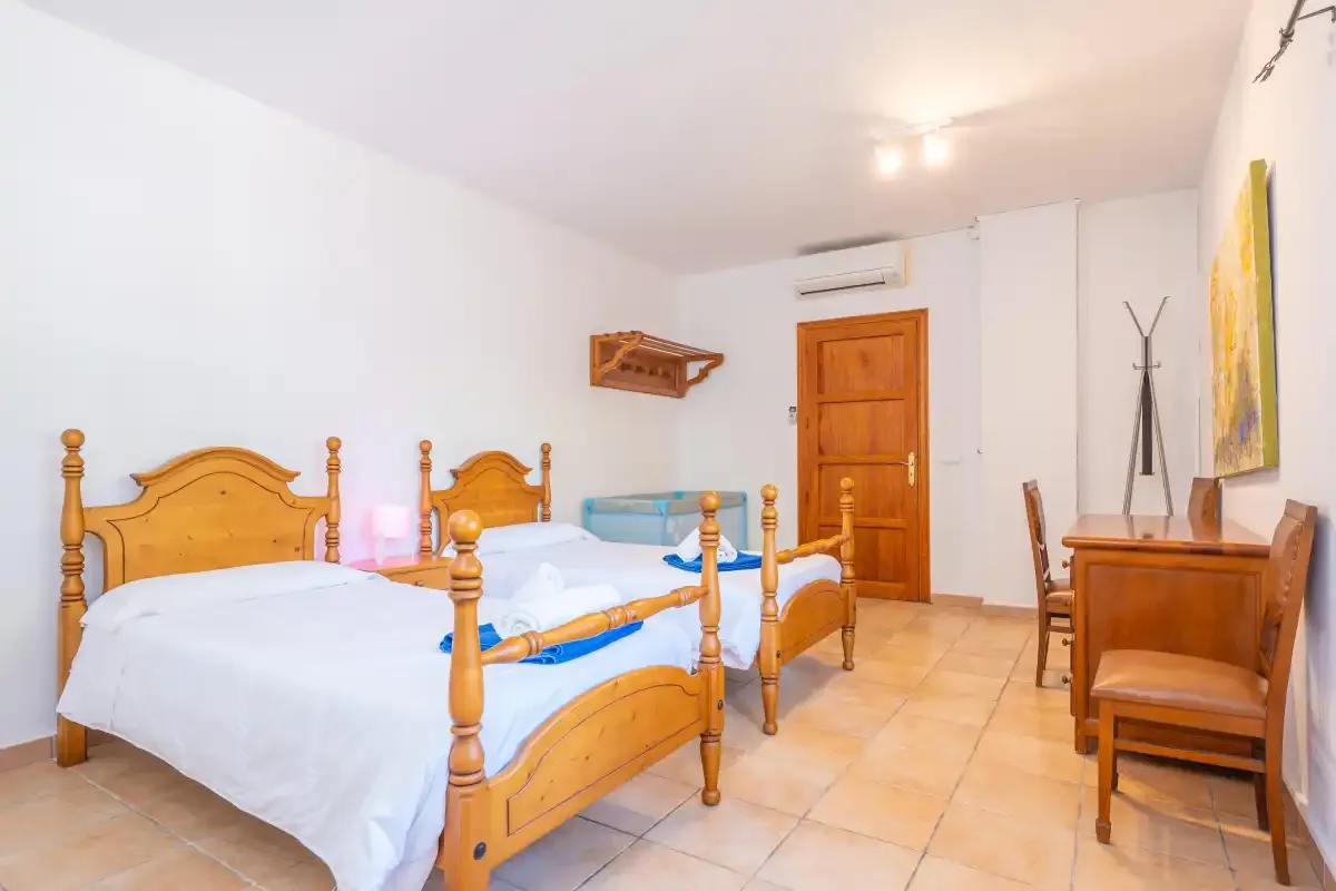 A bedroom with two beds, a wooden desk, and a wall-mounted air conditioner.