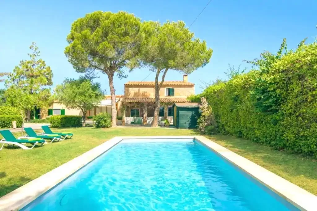 A swimming pool and lawn lead toward a house among trees.
