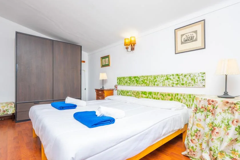 A bright bedroom with white bedding, blue towels, and floral-patterned walls.