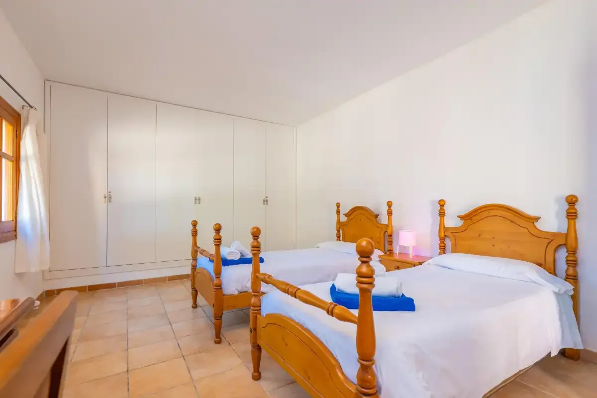 A bedroom with two wooden beds, white linens, and built-in wardrobes.