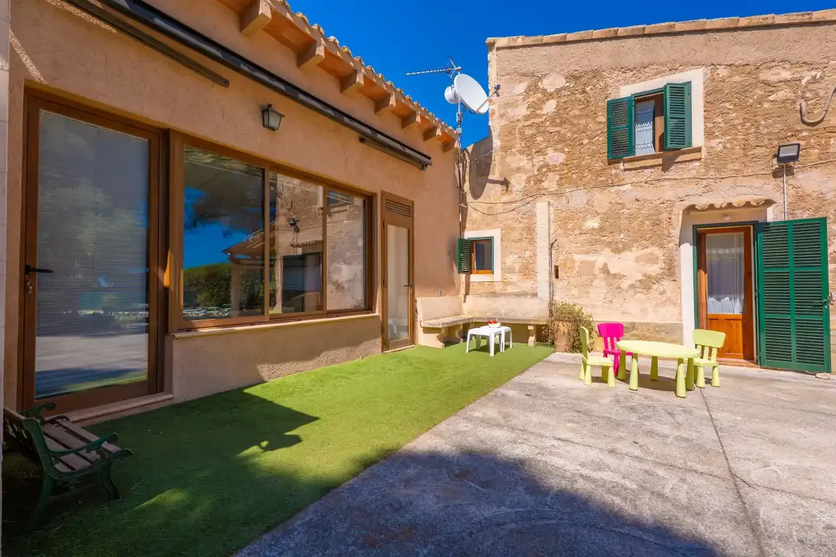 A sunny courtyard with green artificial turf and outdoor seating beside stone buildings.