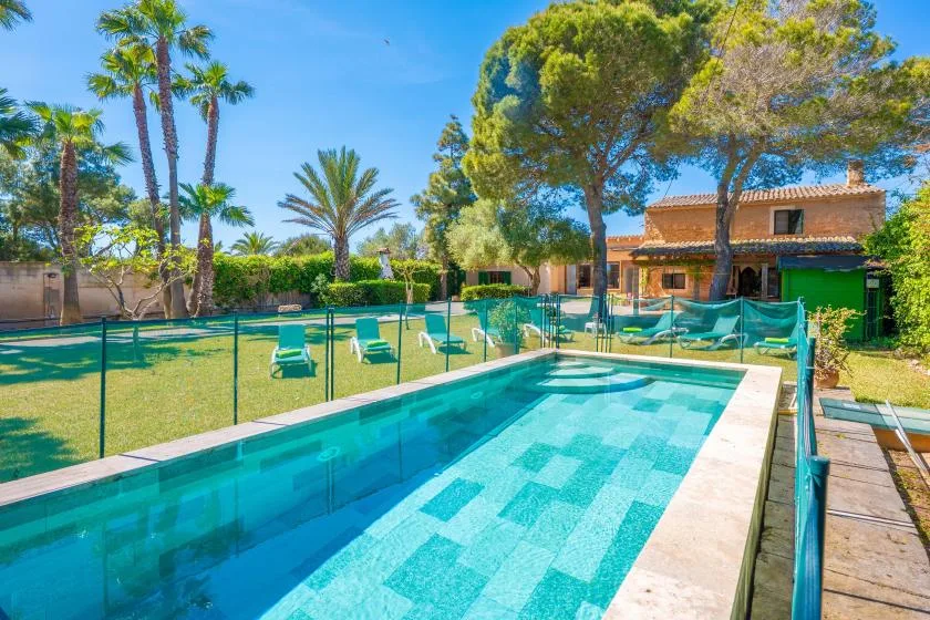 An outdoor swimming pool beside a lawn and a tiled-roof building.