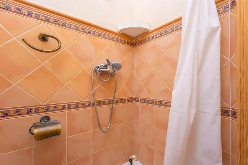 A tiled bathroom shower with a wall-mounted shower fixture and hanging curtain.
