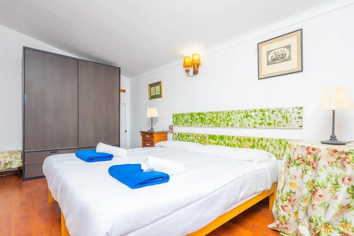 A bedroom with a double bed, blue towels, and floral fabric along the wall.