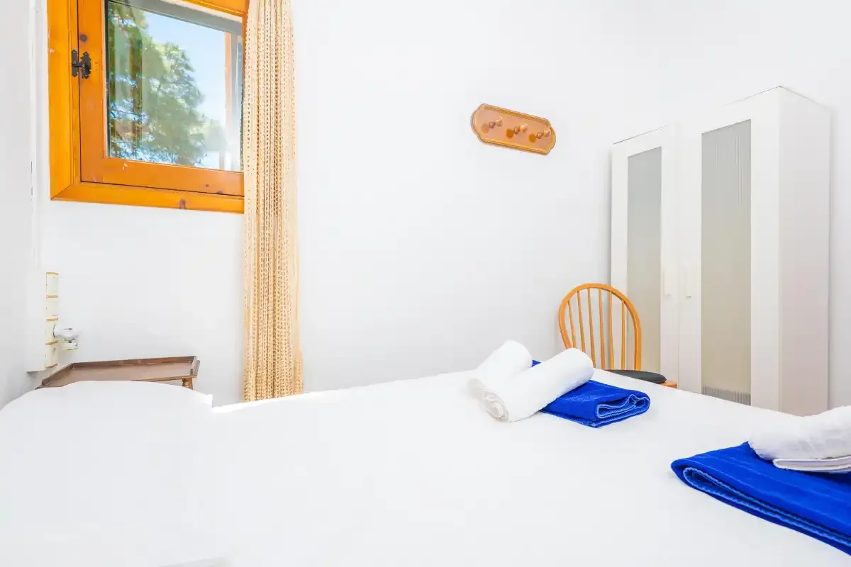 A bright bedroom with white bedding, blue towels, and a window.