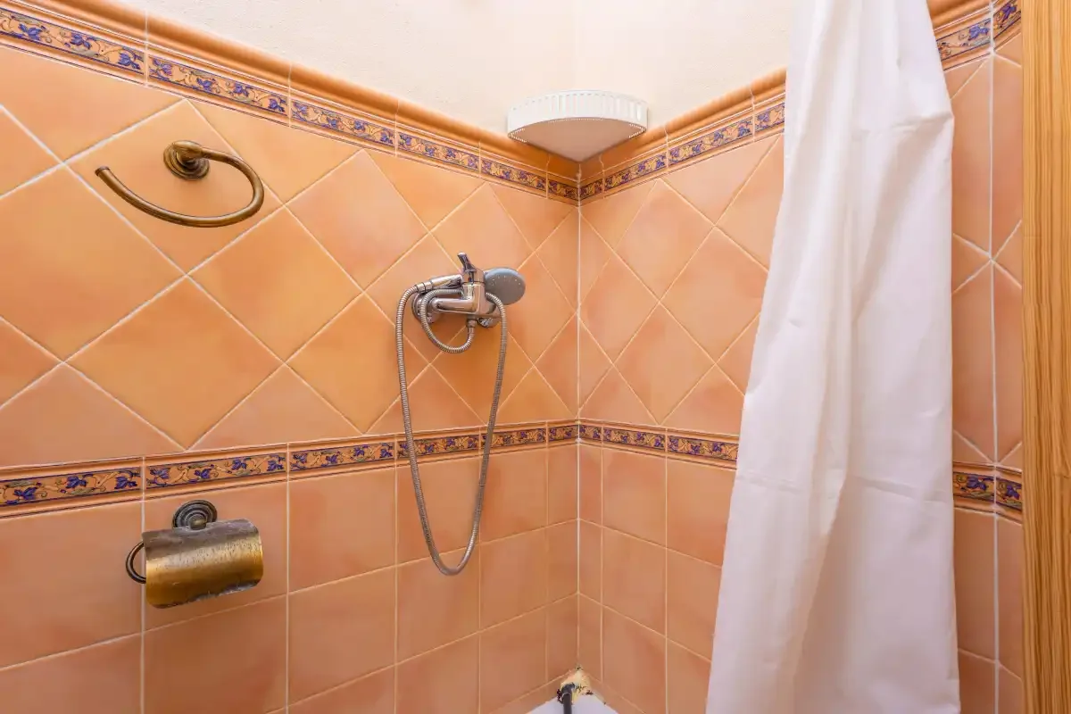 A tiled bathroom shower area with a white curtain.