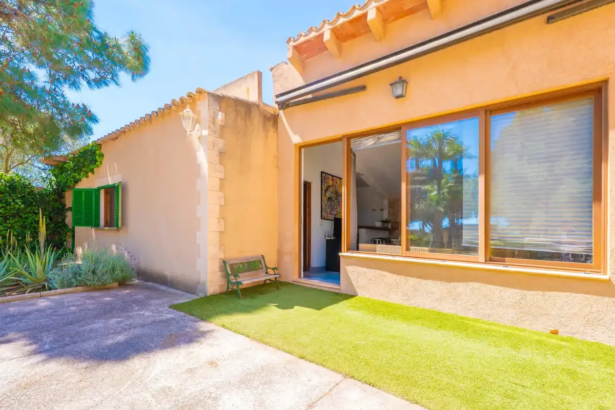 A sunny house exterior with a large window and a small lawn.