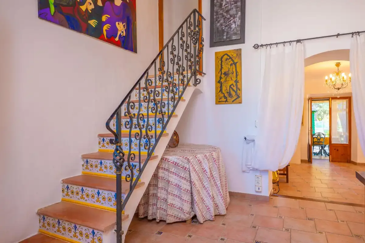 A tiled staircase with a decorative railing rises beside a table in a bright interior.
