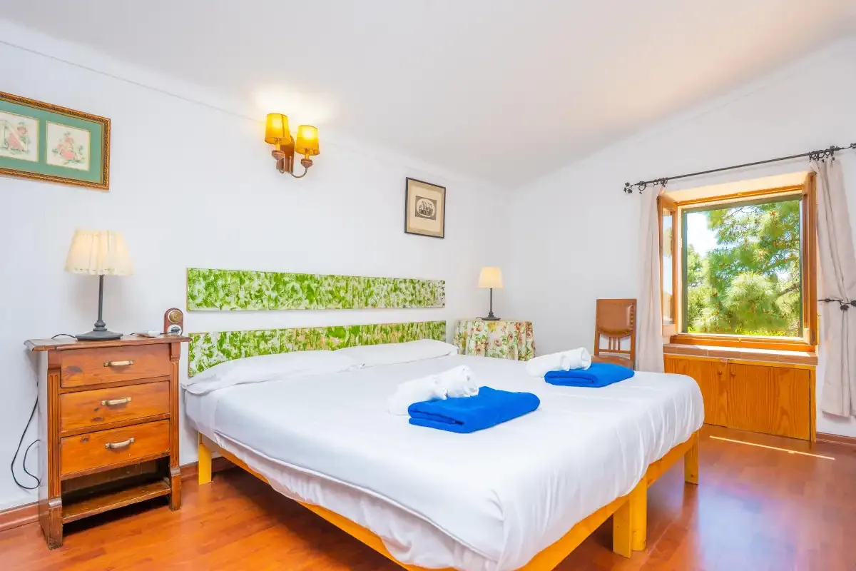 A bedroom with a large bed and a window overlooking greenery.