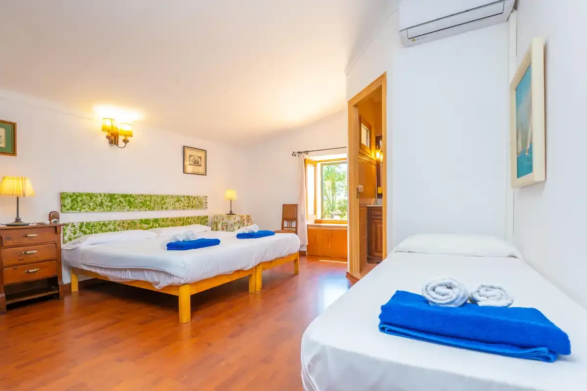 A bedroom with two beds, white bedding, and wooden flooring.