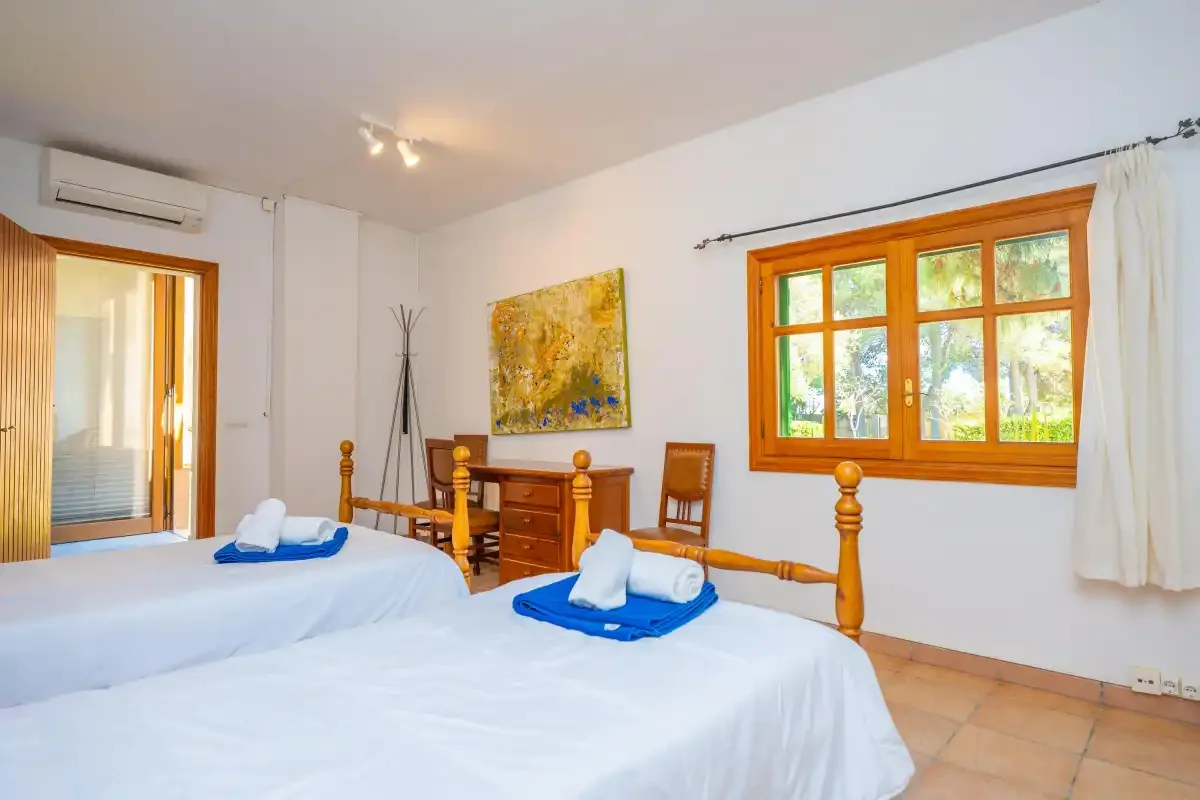 A bedroom with two beds, wooden furniture, and a window overlooking greenery.