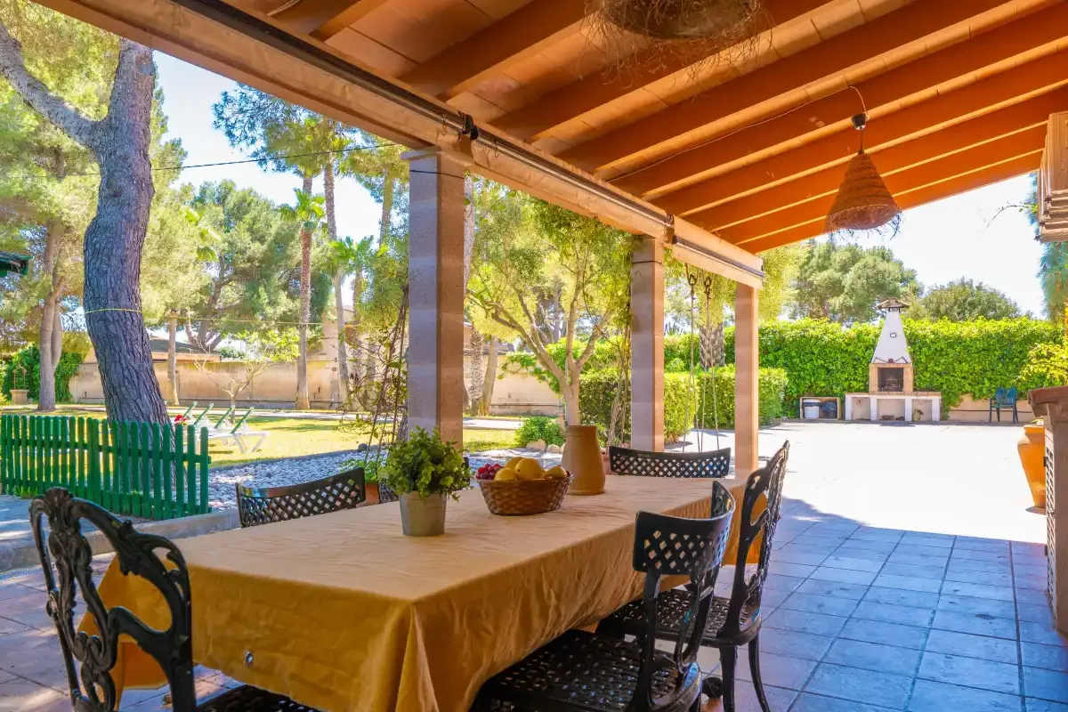 A covered outdoor dining area with a table and chairs overlooks a garden.