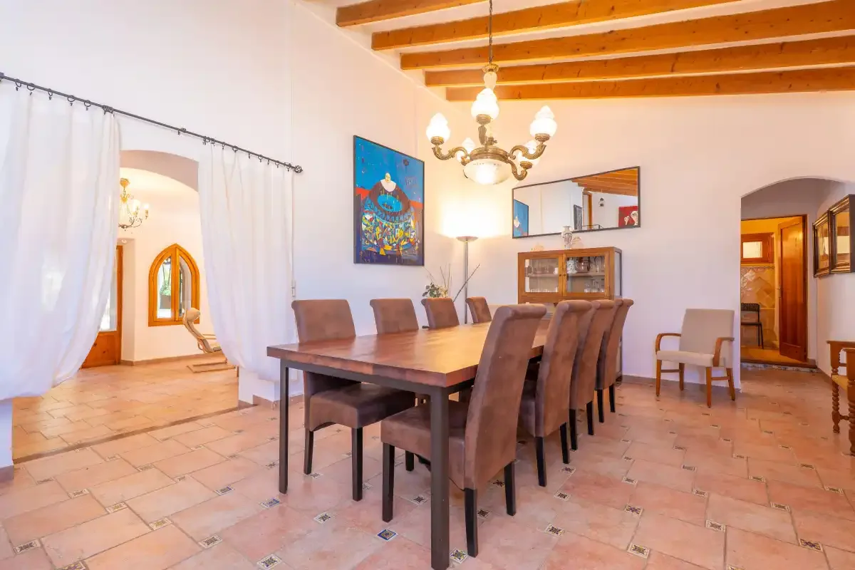 A dining room with a long wooden table and chairs beneath exposed ceiling beams.