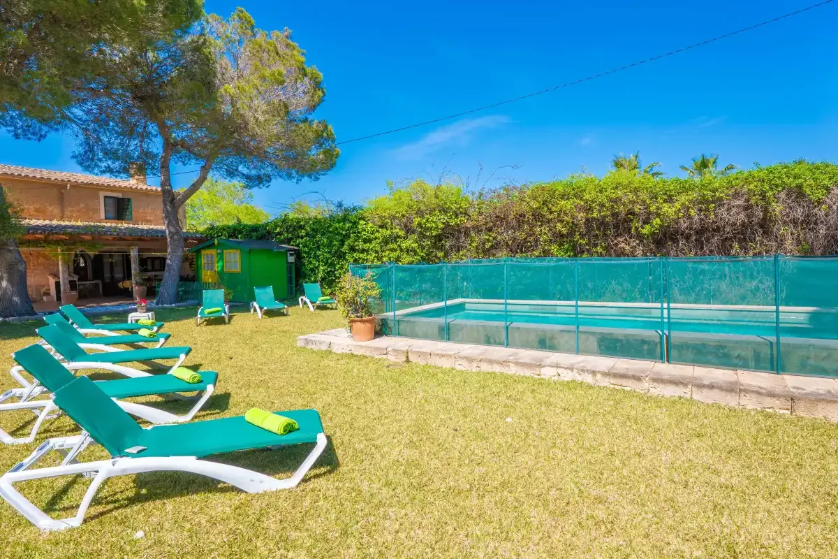 A grassy outdoor pool area has green lounge chairs beside the water.