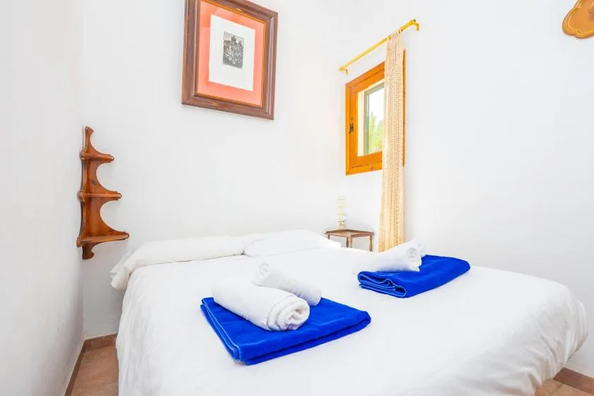 A bright bedroom with a neatly made bed and folded blue towels.
