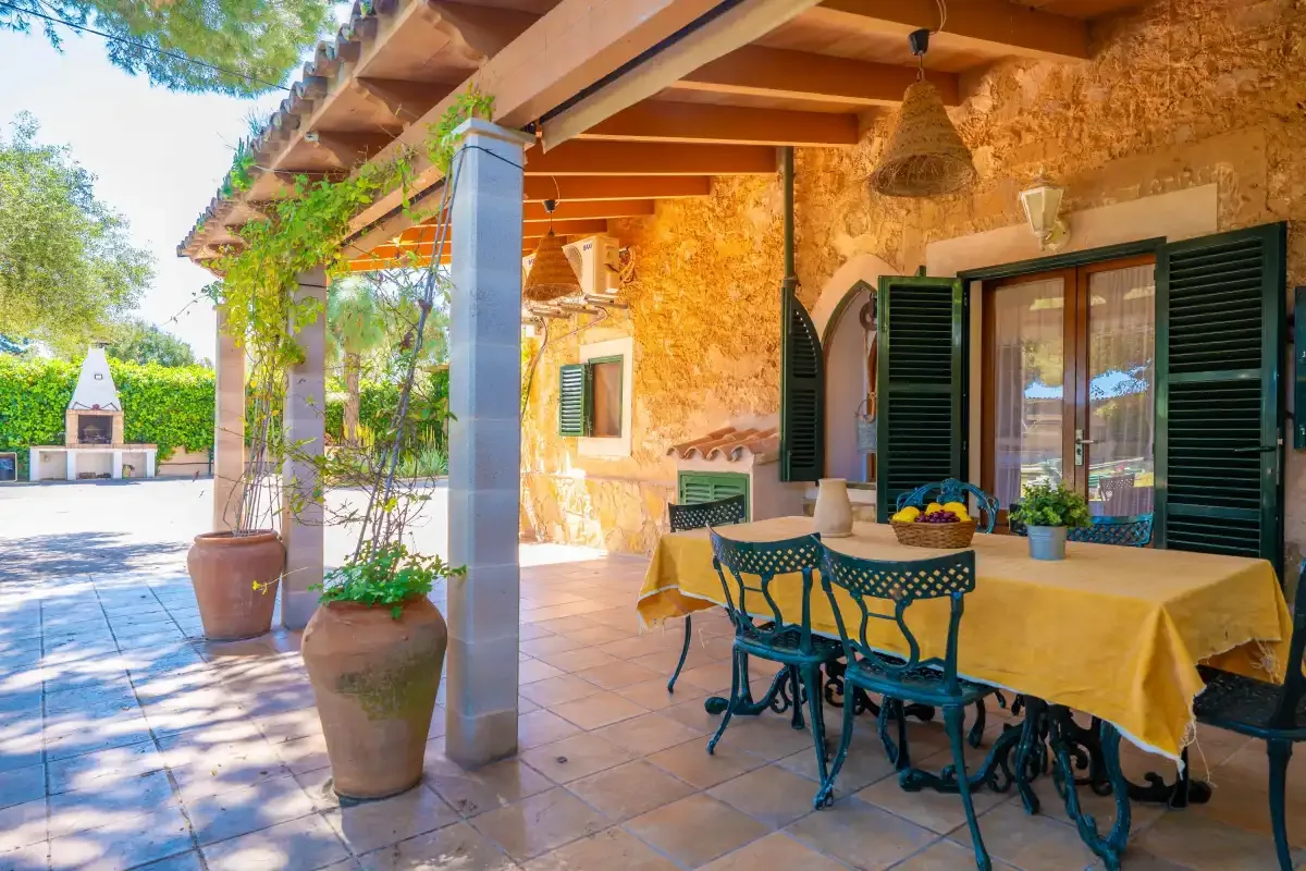 A covered stone patio with a dining table, chairs, and potted plants.