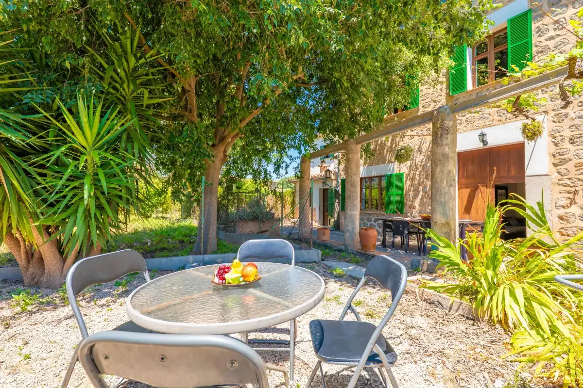 A garden patio with outdoor seating and a round table beside a stone building.