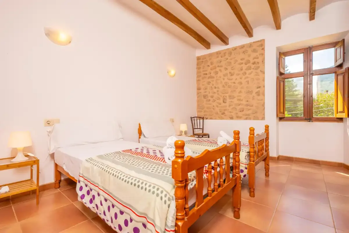 A bedroom with two beds, wooden furnishings, and a window overlooking greenery.