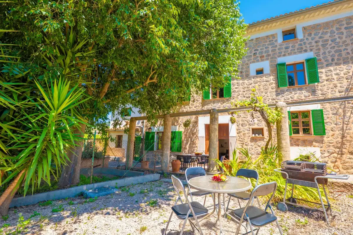 A stone house with green shutters opens onto a garden patio with outdoor seating.