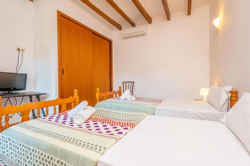 A bedroom with several beds, patterned bedspreads, and exposed wooden ceiling beams.