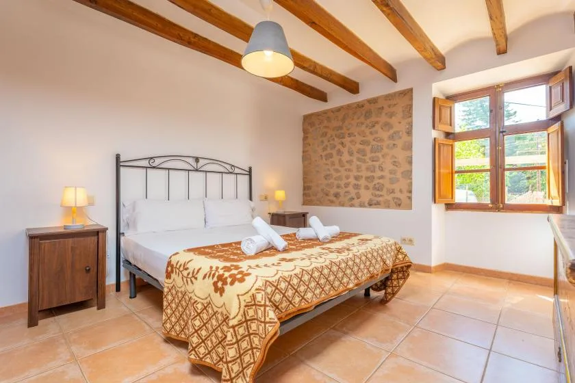 A bedroom with a double bed, exposed wooden ceiling beams, and an open window.