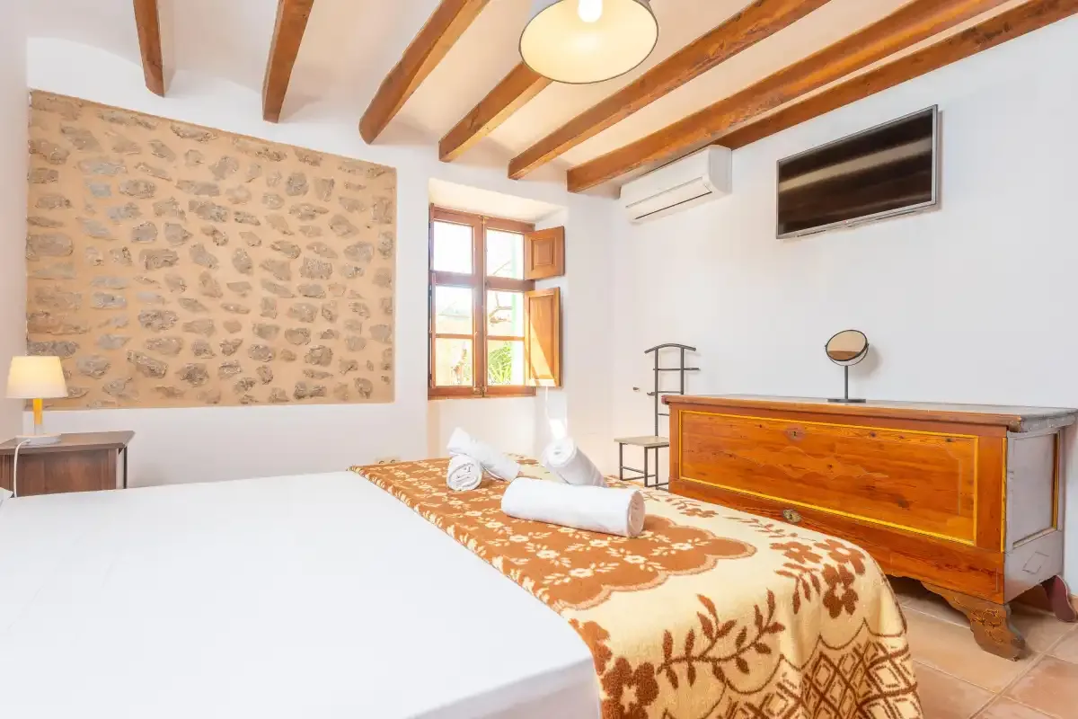 A bedroom with a bed, wooden dresser, and exposed ceiling beams.