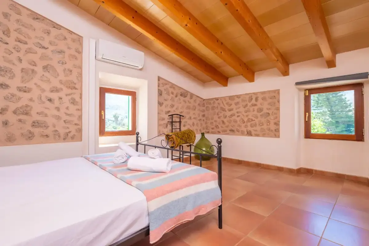A bedroom with two beds, patterned wall panels, and exposed wooden ceiling beams.