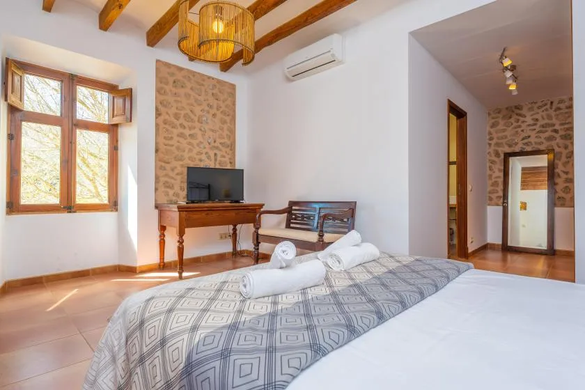 A bedroom with a patterned bedspread, television, and wooden ceiling beams.