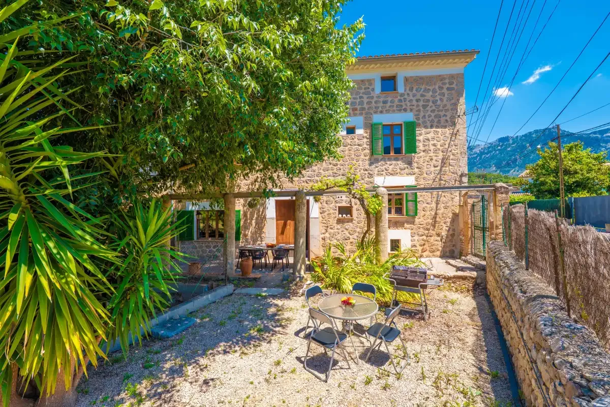 Stone house exterior with a gravel courtyard, outdoor seating, and leafy trees.