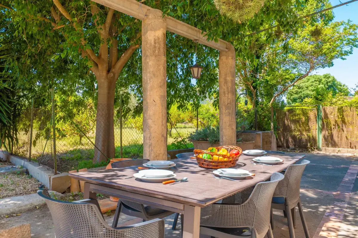 A shaded outdoor dining area with a table set beneath leafy trees.