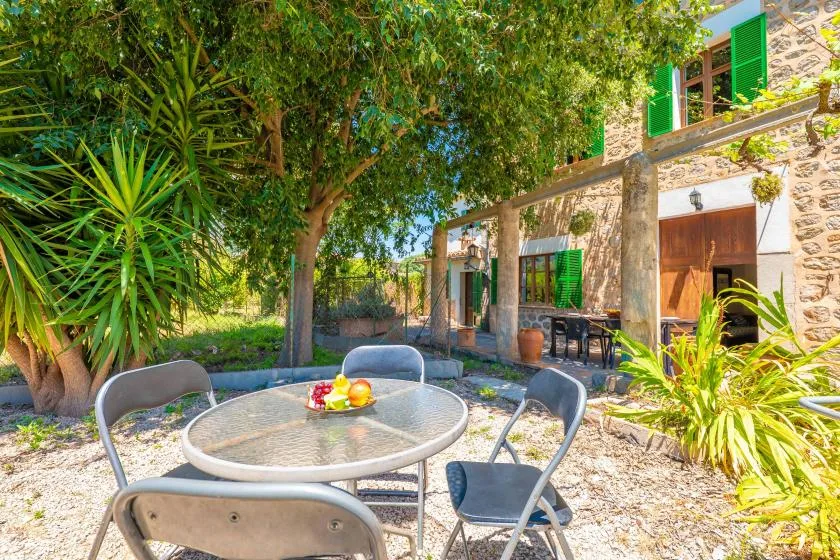 A garden patio with outdoor seating beside a stone building and leafy trees.