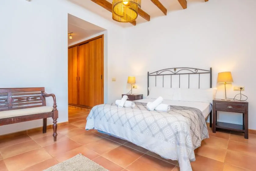 A bedroom with a neatly made bed, bedside tables, and exposed ceiling beams.
