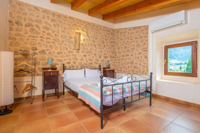 A bedroom with a metal-framed bed, stone-patterned walls, and a window.