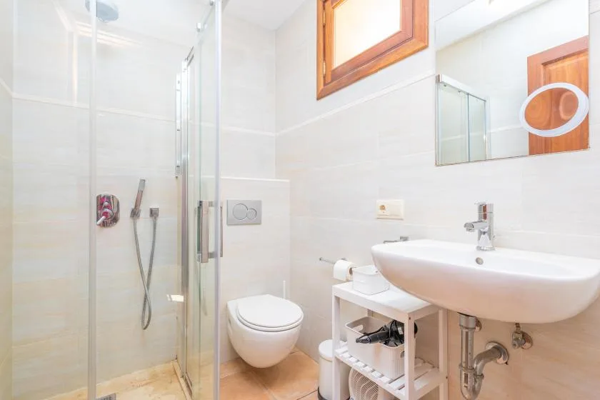 A bright bathroom with a glass shower, wall-mounted toilet, and sink.