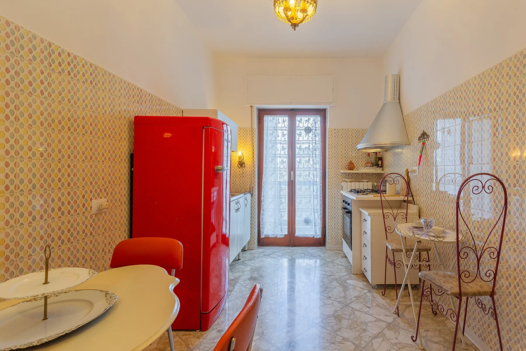 A narrow kitchen with a red refrigerator and glass doors at the far end.