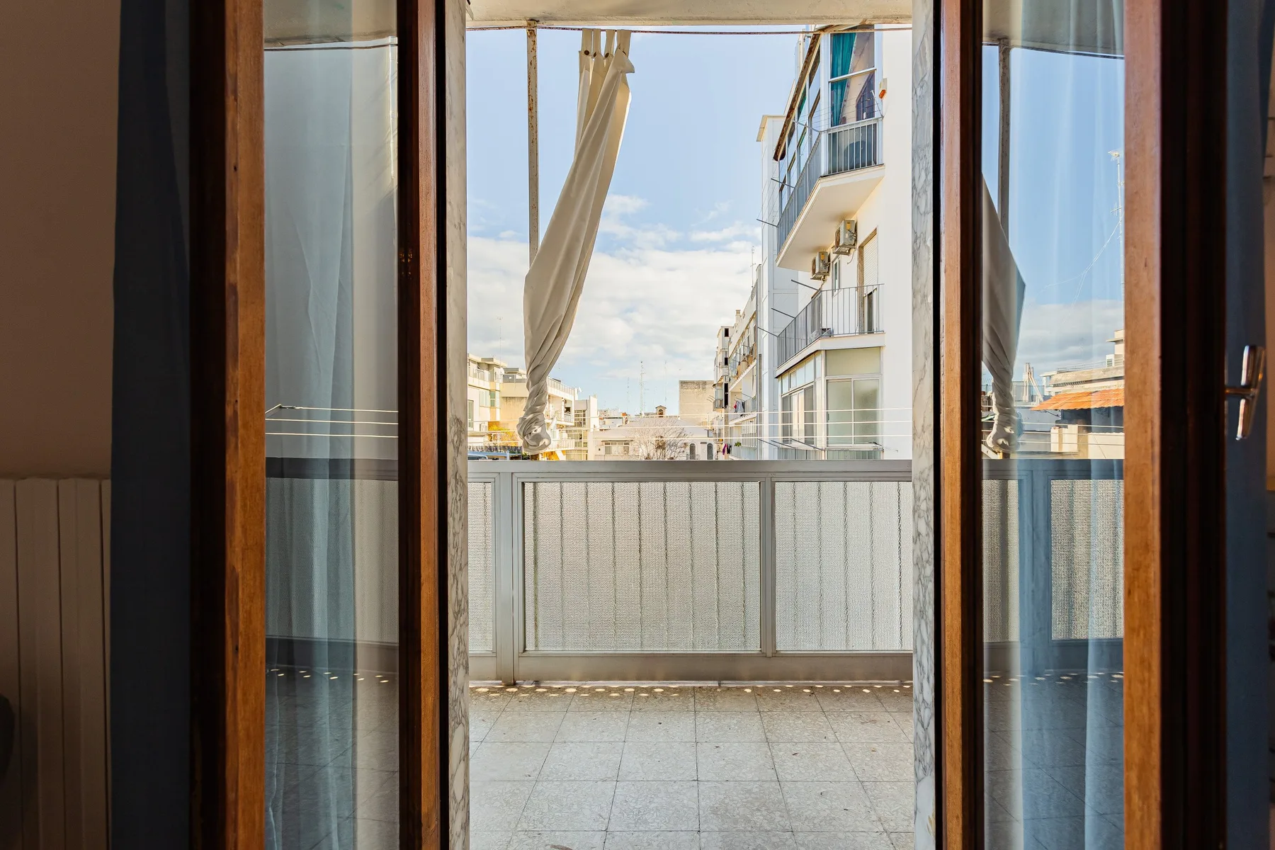 An open balcony doorway looks out onto a balcony with neighboring buildings beyond.