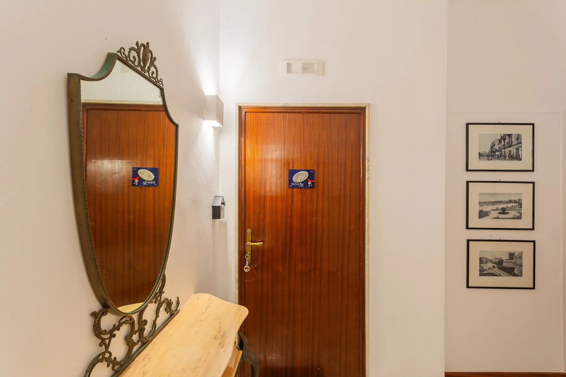 An indoor hallway with a wooden door, a wall mirror, and framed pictures.