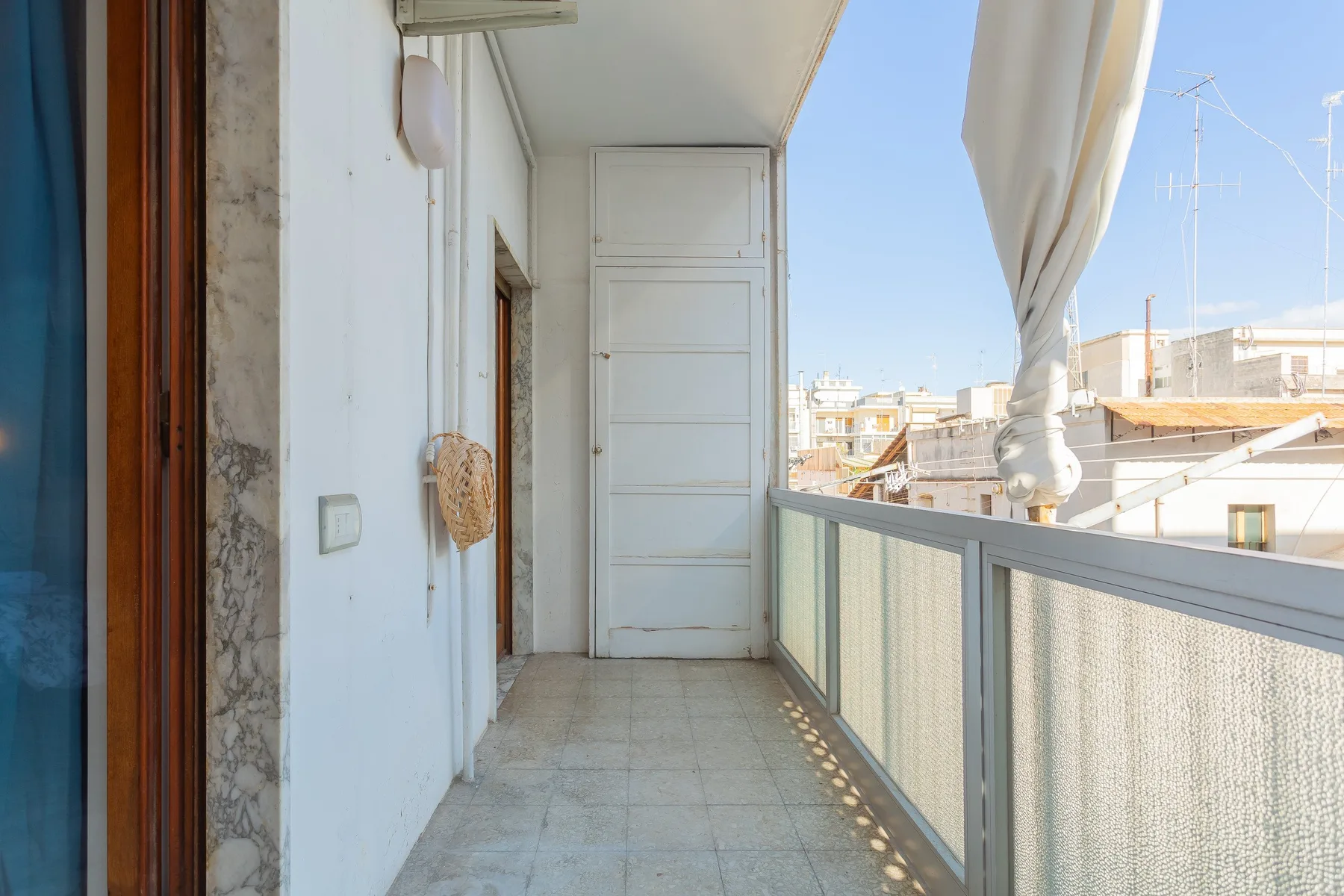 A narrow balcony with a tiled floor and a railing overlooking nearby buildings.