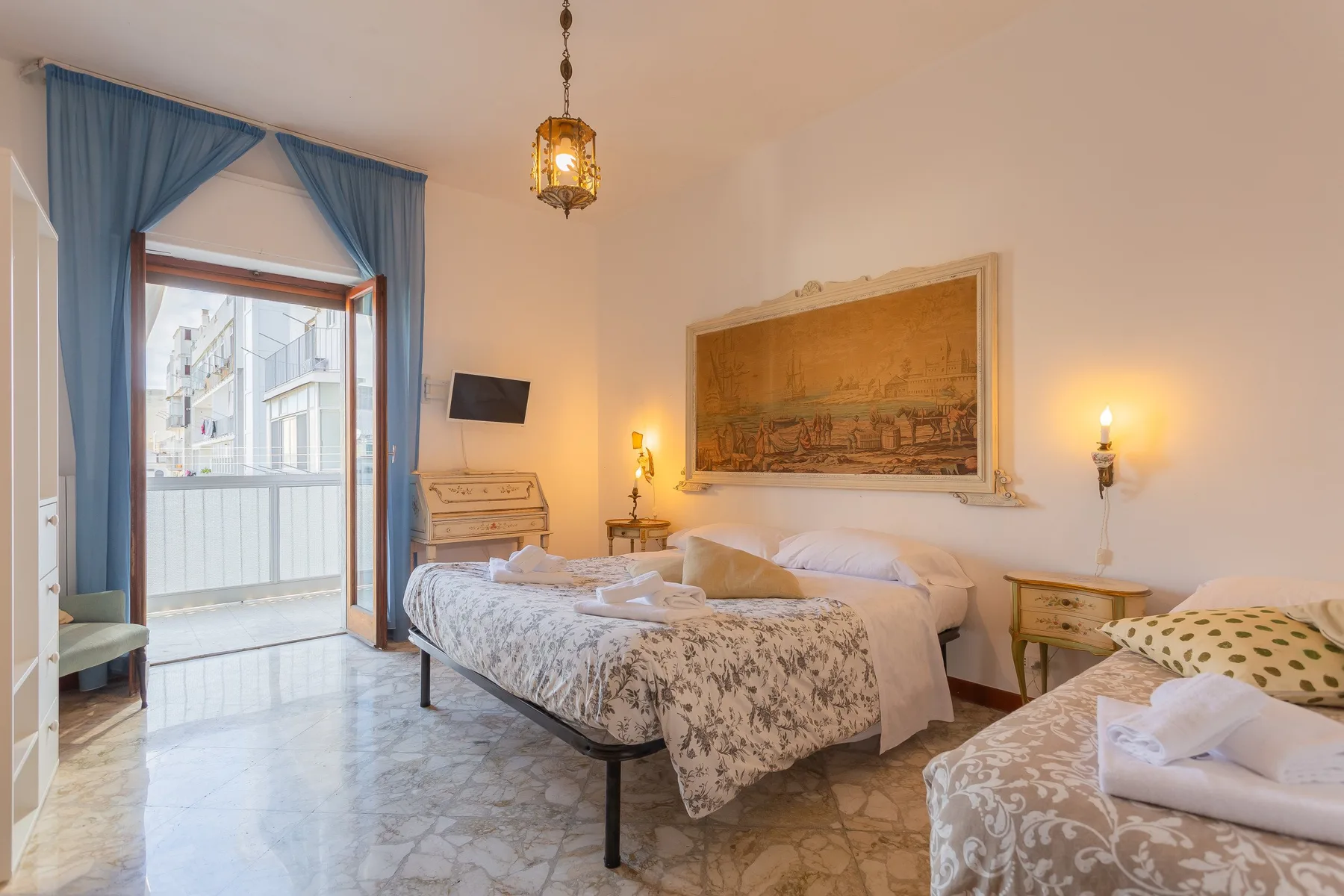 A bright bedroom with beds, blue curtains, and a balcony door.