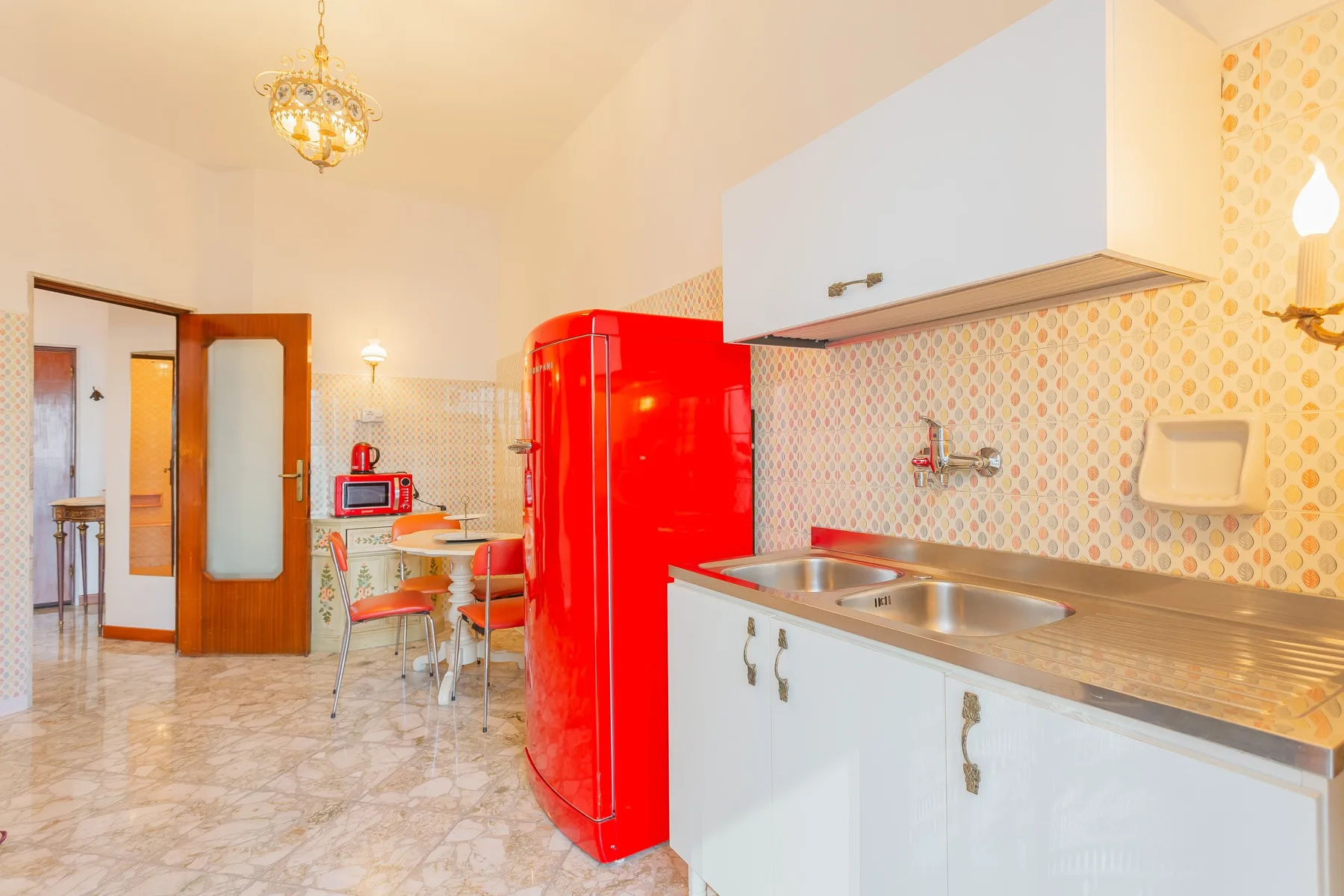 A bright kitchen with white cabinetry, patterned tile, and a red refrigerator.