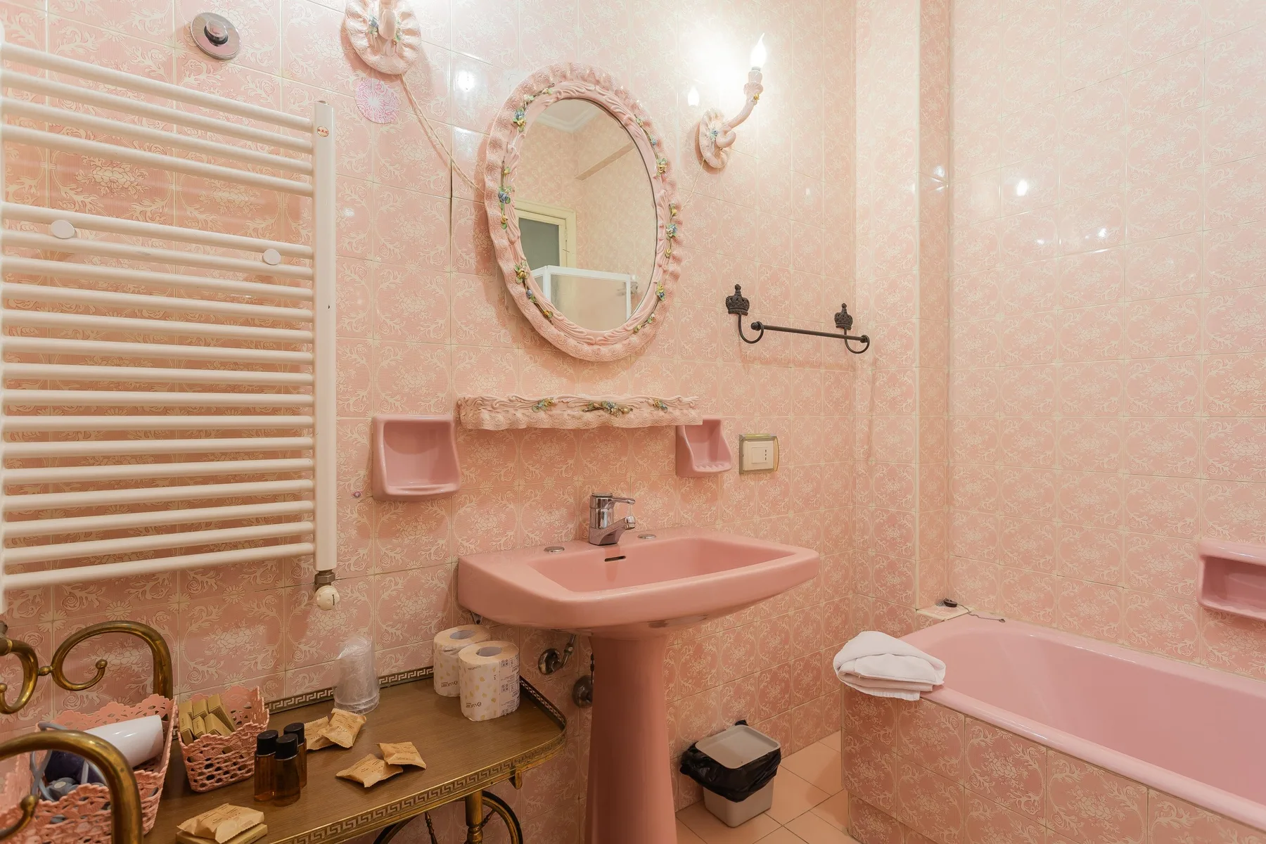 A pink-tiled bathroom with a pedestal sink and bathtub.