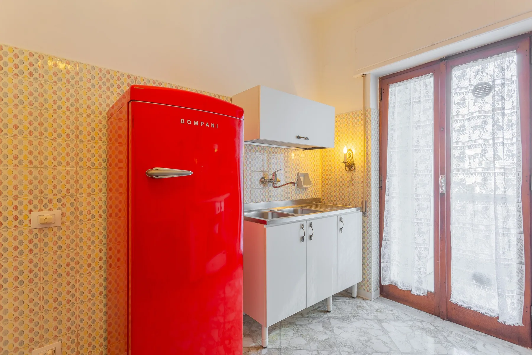A compact kitchen with a red refrigerator, white cabinets, and a glass door.