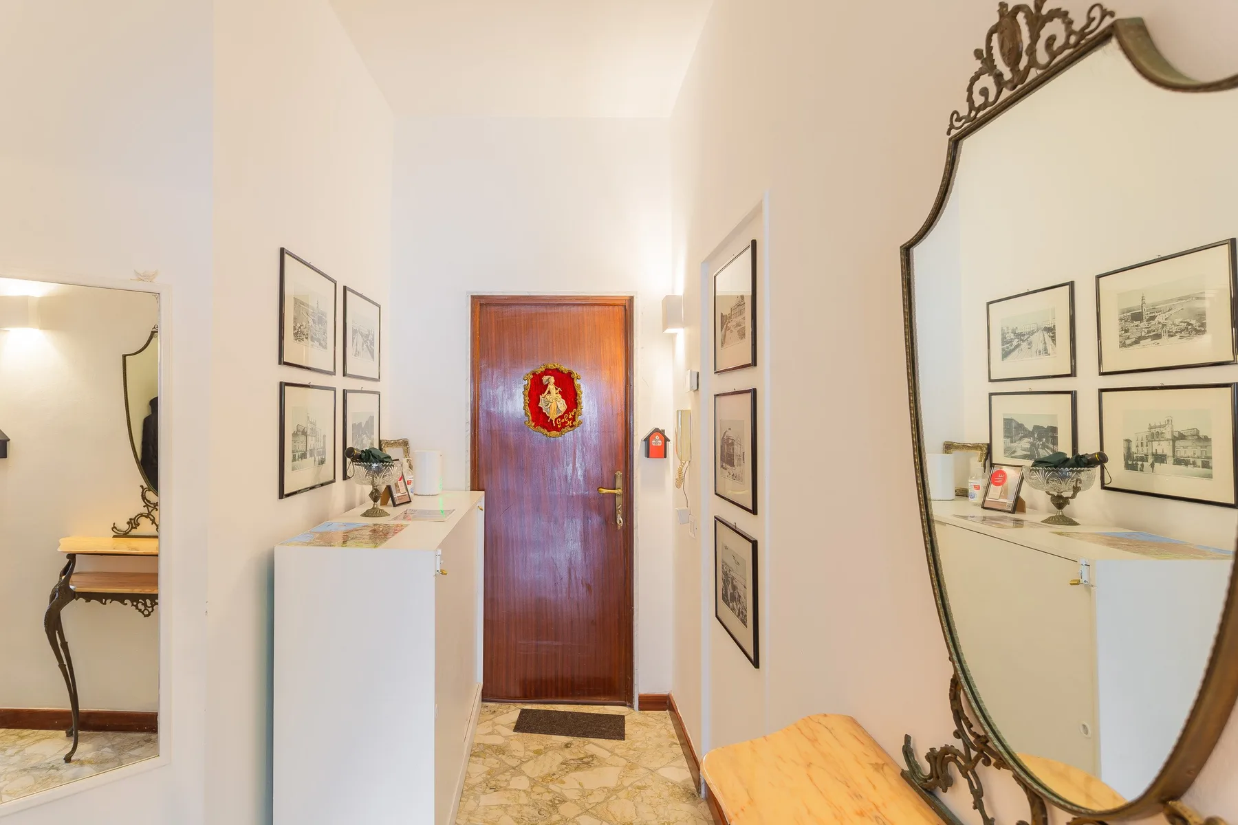 Un recibidor luminoso con una puerta de madera, cuadros enmarcados y un espejo grande.