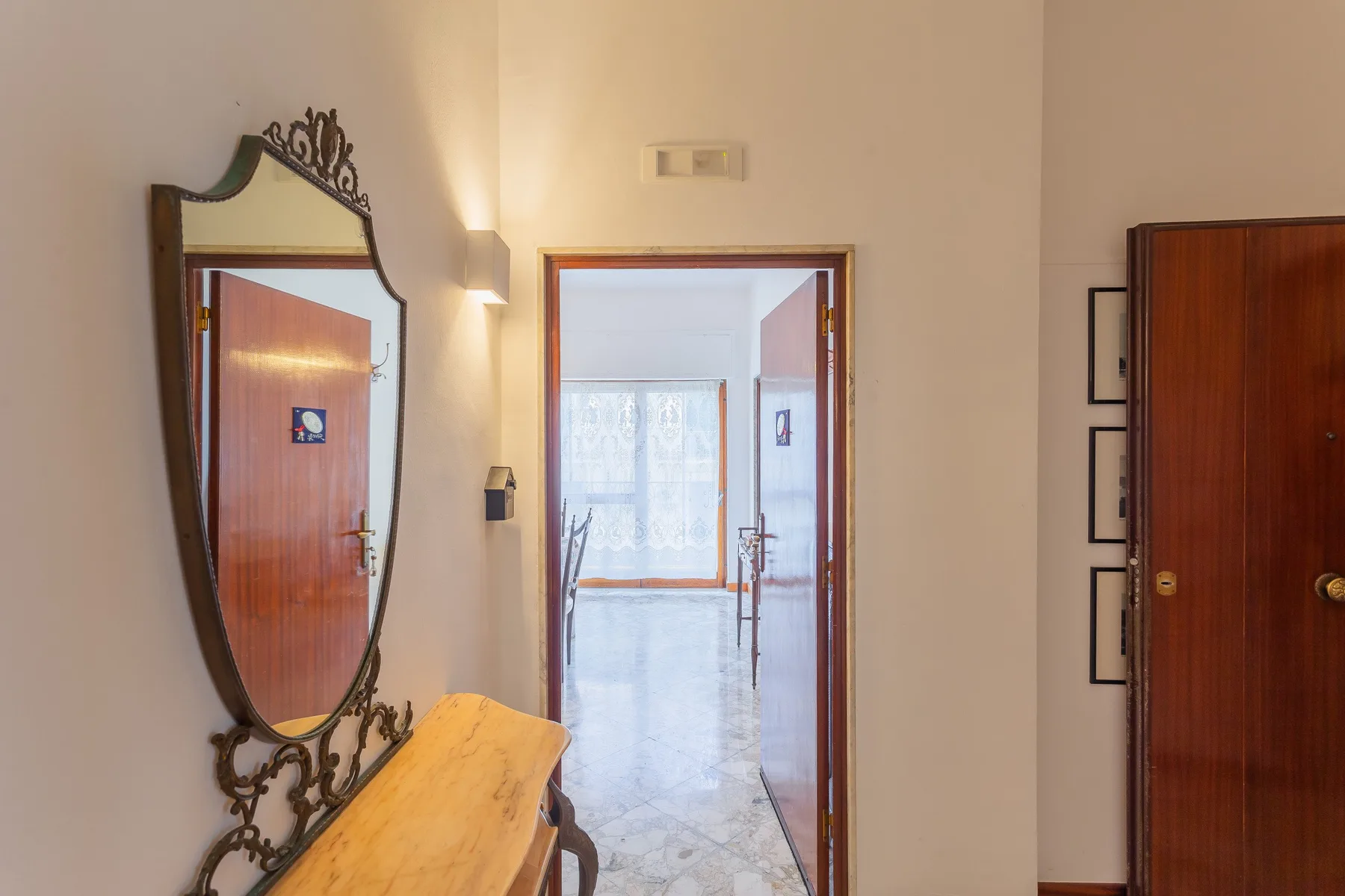 An interior hallway opens into a bright room with a window and sheer curtains.